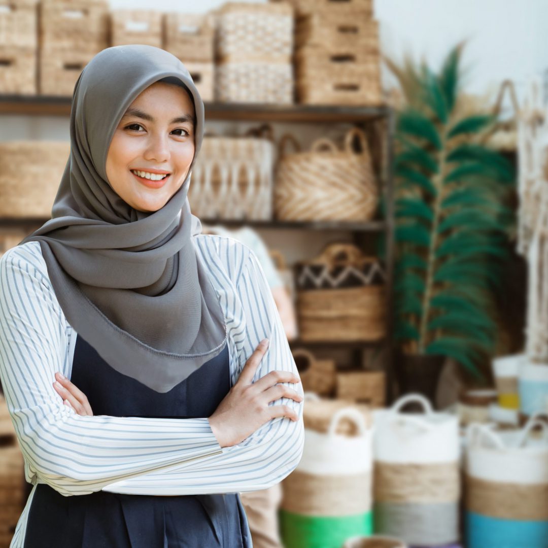 young muslim woman stand with crossed hands among handicraft items in craft galleries. business of asian woman with head scarf at shop